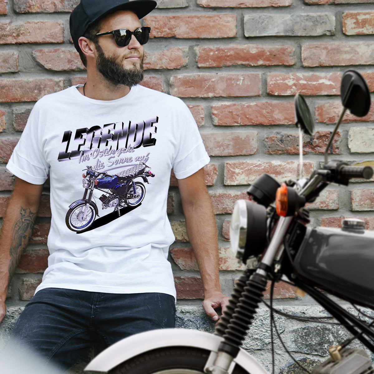 Mann mit weißem Simson "Legende" T-Shirt, lehnt an einer Wand. Im Vordergrund eine schwarze Simson S51
