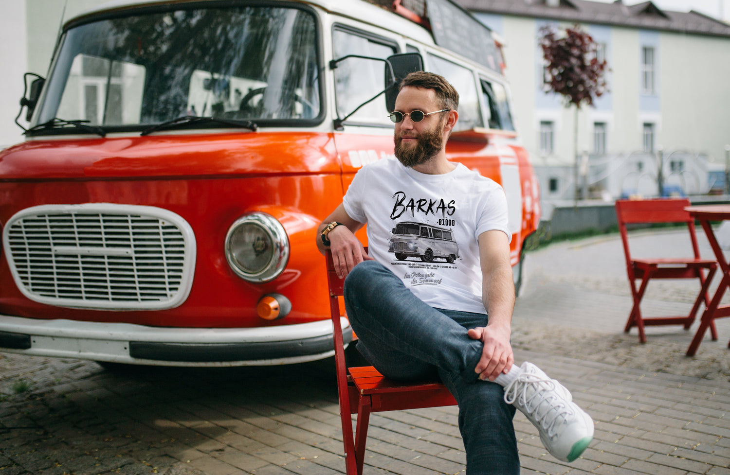 Ein Mann mit lässigem weißen Barkas-T-Shirt sitzt vor einem roten Barkas B1000.