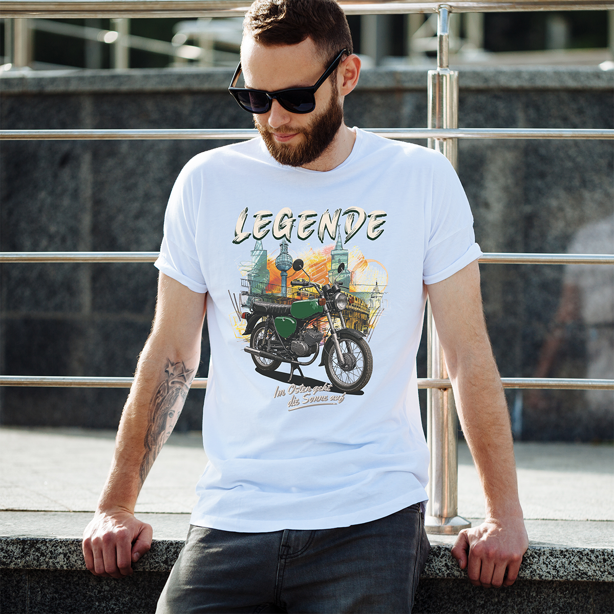 Mann mit weißem "Legende" T-Shirt, lehnt sich an ein Geländer.