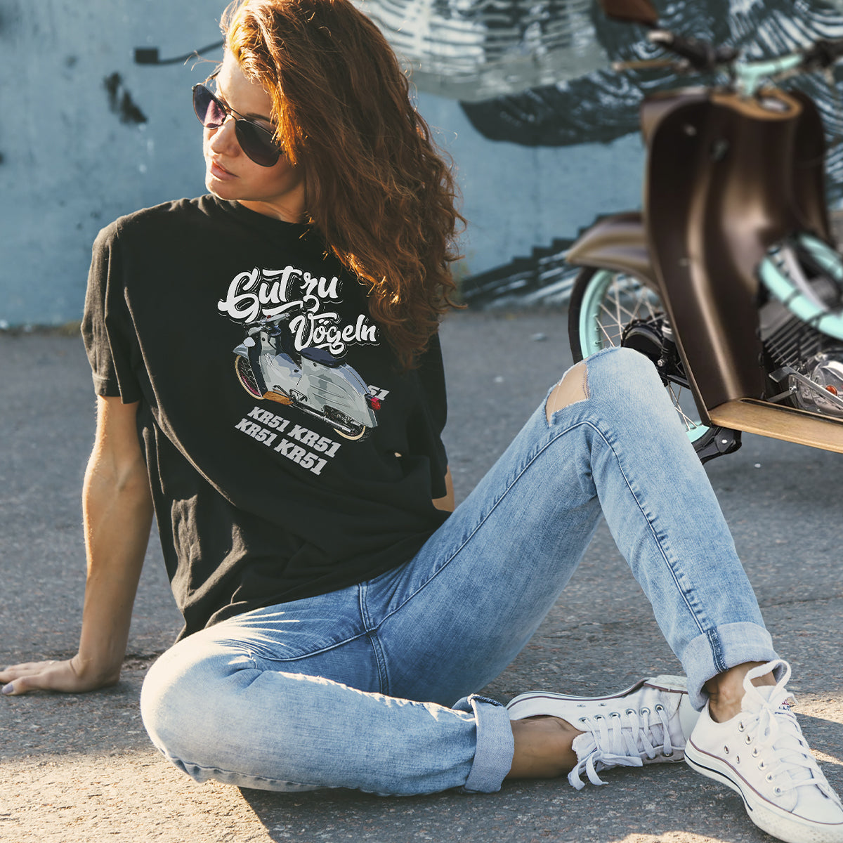 Junge Frau mit schwarzer Sonnenbrille und schwarzem T-Shirt "Gut zu Vögeln" posiert vor einer Simson-Schwalbe.